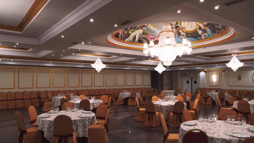 Salón con arañas y mural en techo, mesas redondas para banquete.