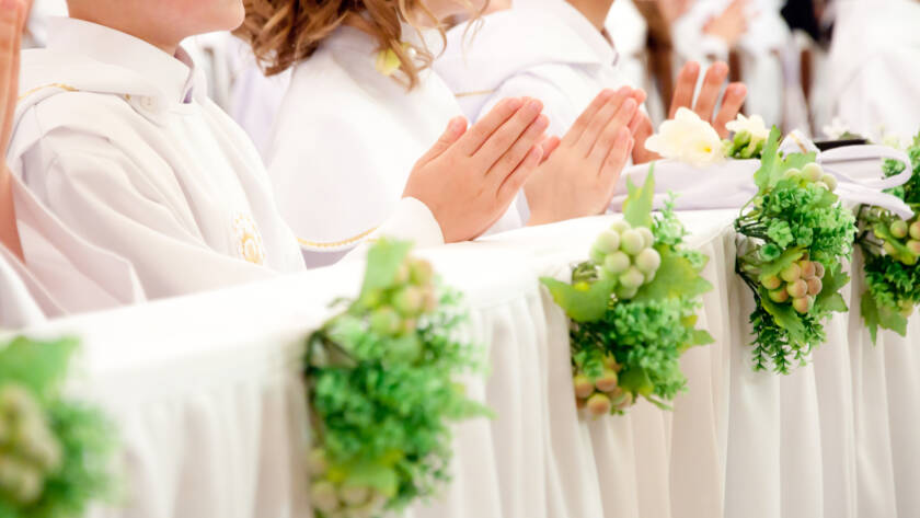 Fila de niños en comunión, oración frente a mesa con flores y hiedra.