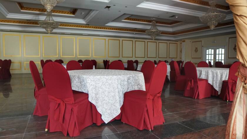 Salón de banquetes con mesas redondas y manteles blancos; sillas con fundas rojas