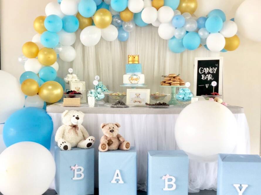 Candy bar de baby shower con arco de globos azules y dorados y bloques BABY.