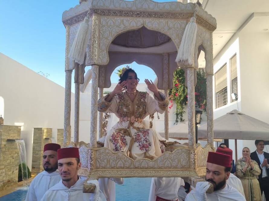 Novia en palanquín tradicional portada por acompañantes con fez rojo.