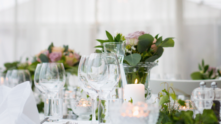 Mesa de boda con copas, vela encendida y centro floral en verde y rosa.